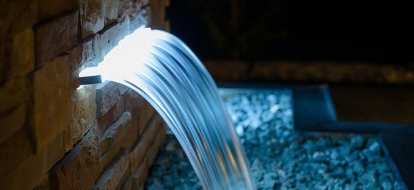 Waterfall landscape feature pouring onto stones with blue lighting at water entrance. 